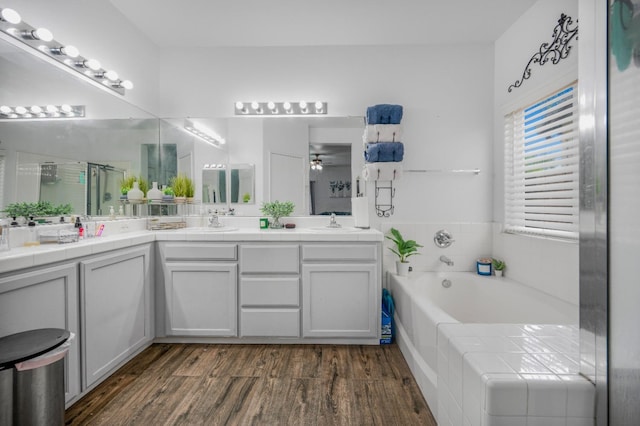 full bathroom with wood finished floors, double vanity, a ceiling fan, a sink, and a bath