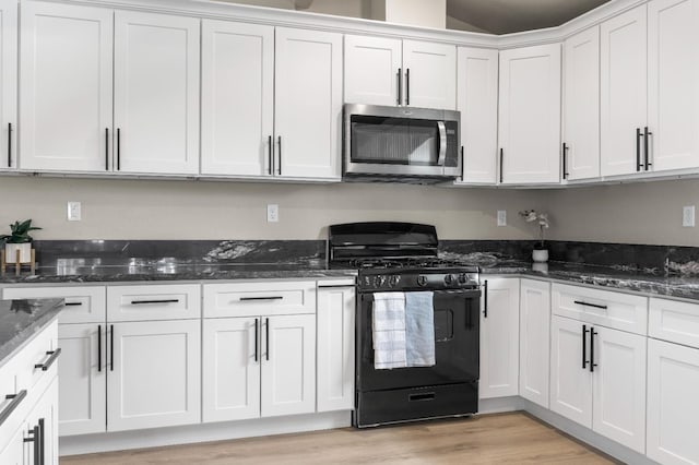3659 Mono St, Fresno, CA 93702 - kitchen with stainless steel microwave, black gas range oven, white cabinetry, light wood-style floors, and dark stone counters