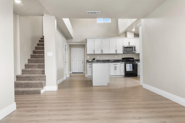 3659 Mono St, Fresno, CA 93702 - kitchen featuring black gas range, stainless steel microwave, white cabinetry, open floor plan, and high vaulted ceiling