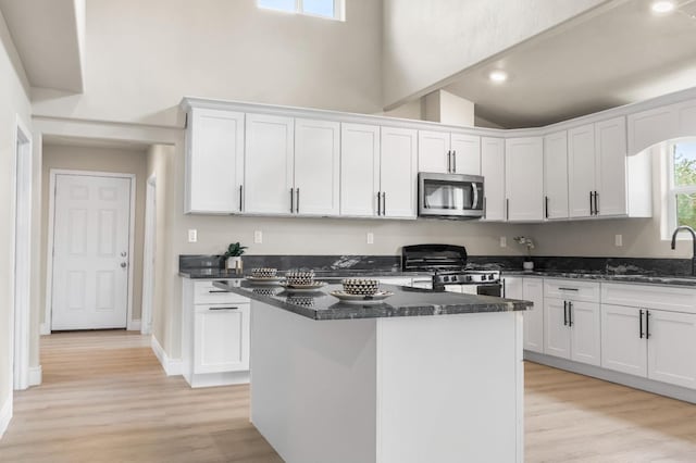 3659 Mono St, Fresno, CA 93702 - kitchen featuring stainless steel microwave, gas range oven, white cabinets, high vaulted ceiling, and light wood finished floors