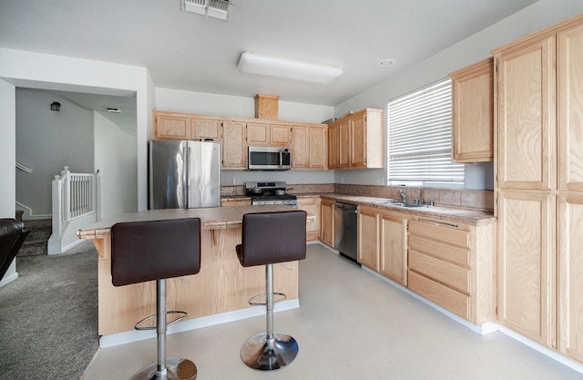 kitchen featuring light brown cabinetry, stainless steel appliances, a breakfast bar, visible vents, and a sink