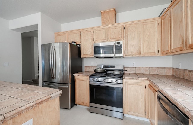 kitchen with tile counters, light brown cabinets, and stainless steel appliances