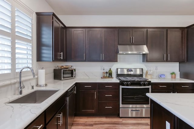 kitchen with light stone counters, dark brown cabinets, a sink, appliances with stainless steel finishes, and under cabinet range hood