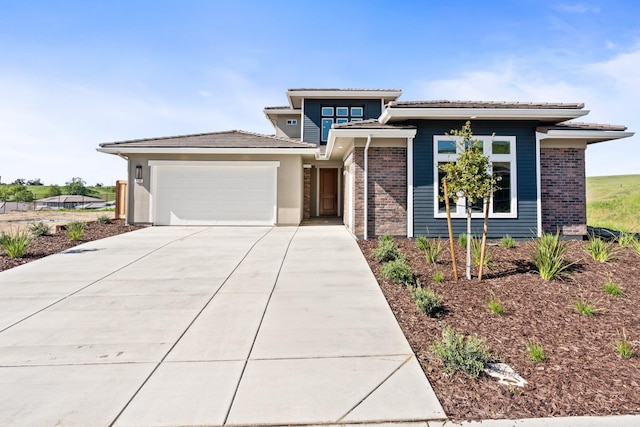 prairie-style house with concrete driveway, a tiled roof, brick siding, and a garage