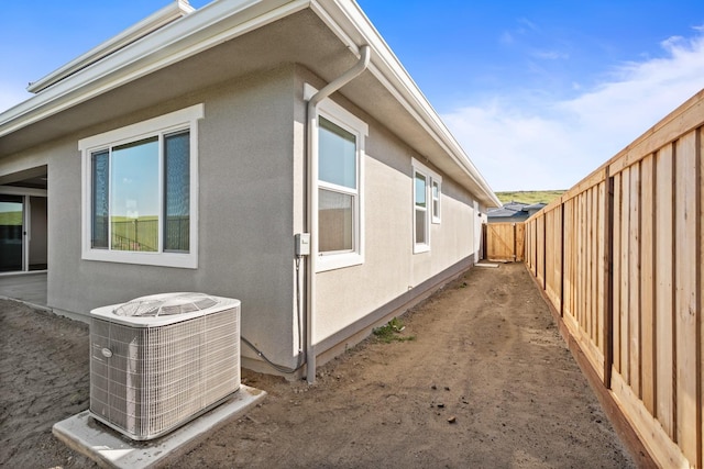 view of side of home with a fenced backyard, central AC, and stucco siding