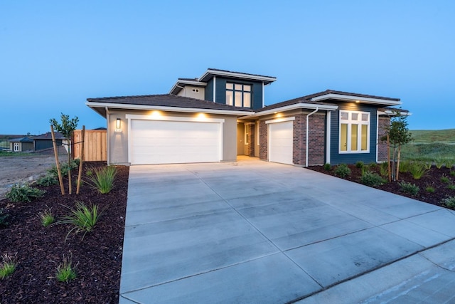 prairie-style home with brick siding, an attached garage, driveway, and fence