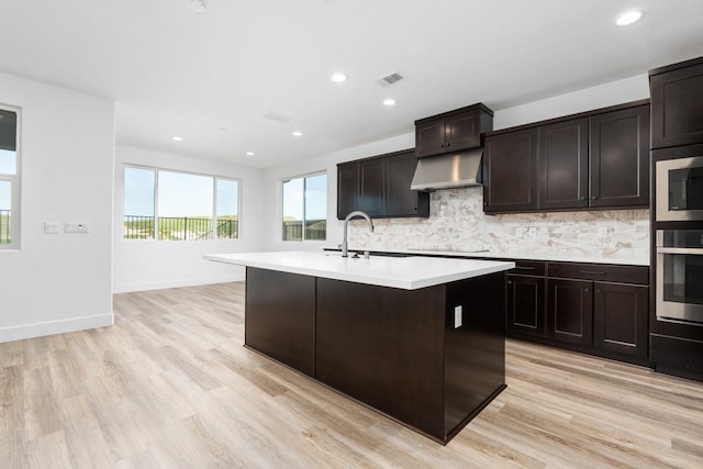 kitchen with a sink, appliances with stainless steel finishes, light countertops, backsplash, and under cabinet range hood
