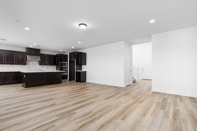 kitchen with under cabinet range hood, backsplash, visible vents, stainless steel microwave, and a kitchen island