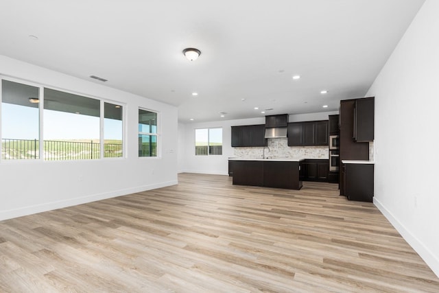 kitchen with stainless steel microwave, open floor plan, visible vents, wall chimney range hood, and light countertops