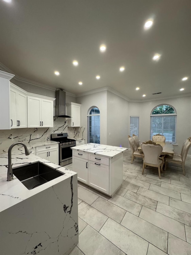 5357 E Burns, Fresno, CA 93725 - kitchen featuring stainless steel gas stove, wall chimney range hood, ornamental molding, a center island, and decorative backsplash