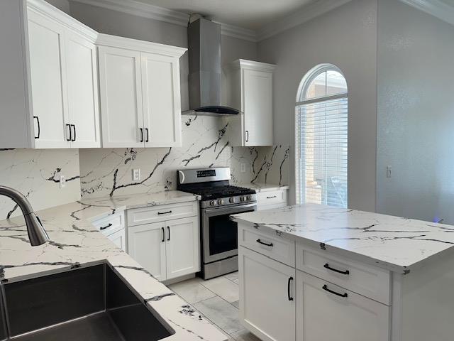 5357 E Burns, Fresno, CA 93725 - kitchen featuring stainless steel gas range oven, wall chimney exhaust hood, white cabinets, light stone counters, and ornamental molding