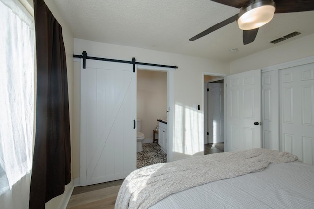 bedroom featuring a barn door, ensuite bathroom, light wood-style floors, ceiling fan, and visible vents