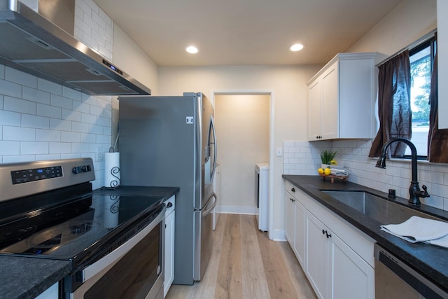 kitchen with wall chimney range hood, a sink, light wood-style flooring, appliances with stainless steel finishes, and white cabinetry