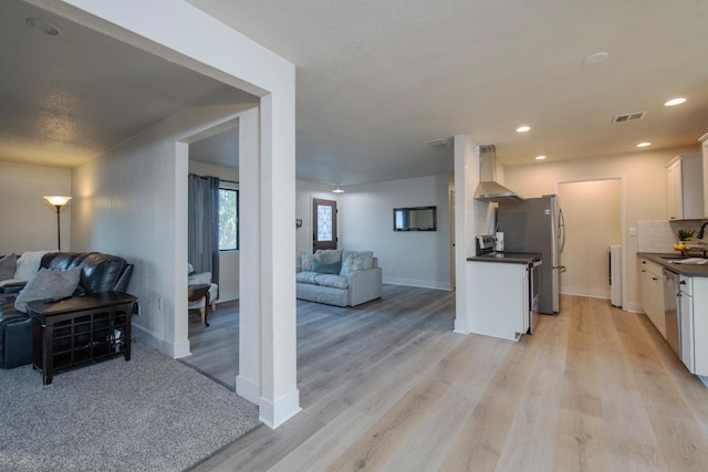 kitchen featuring wall chimney exhaust hood, open floor plan, visible vents, and dark countertops