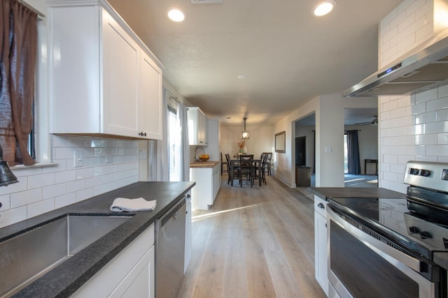 kitchen featuring white cabinets, backsplash, wall chimney range hood, a sink, and appliances with stainless steel finishes