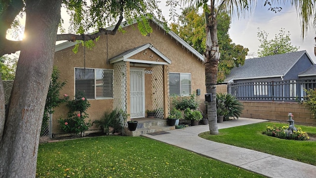 bungalow-style home with fence, a front yard, and stucco siding
