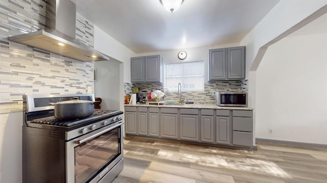kitchen with a sink, wall chimney range hood, backsplash, gray cabinets, and appliances with stainless steel finishes