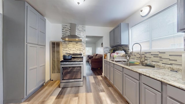 kitchen featuring gray cabinets, wall chimney range hood, a sink, and stainless steel gas stove