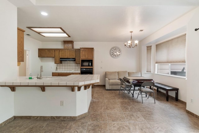 kitchen with a sink, tile countertops, black appliances, brown cabinets, and a peninsula
