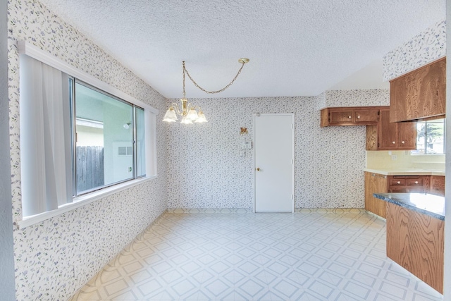 unfurnished dining area featuring light floors, a chandelier, wallpapered walls, and a textured ceiling