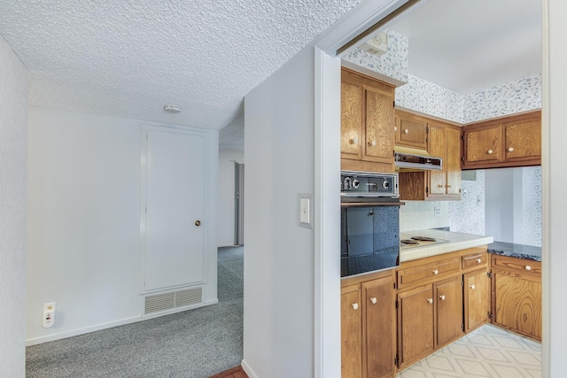 kitchen with brown cabinets, visible vents, oven, and under cabinet range hood