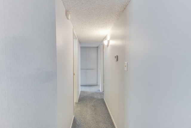 hall featuring carpet floors, a textured ceiling, and baseboards