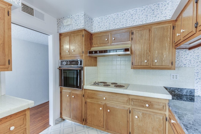 kitchen featuring under cabinet range hood, backsplash, visible vents, black oven, and white electric stovetop