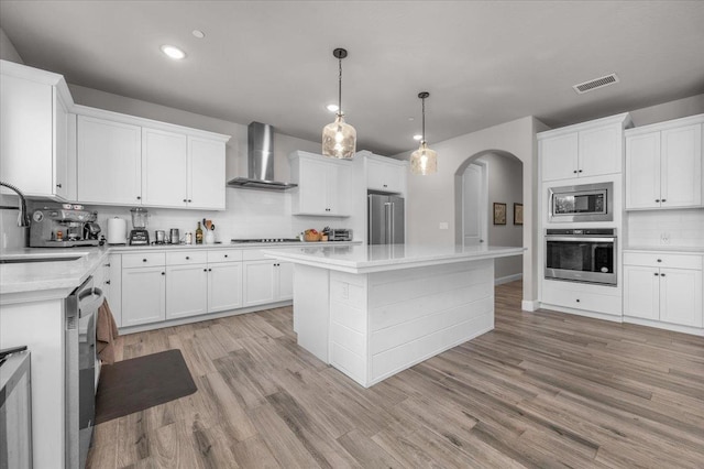 2653 Vermont Ave, Clovis, CA 93619 - kitchen featuring stainless steel appliances, wall chimney exhaust hood, arched walkways, decorative backsplash, and light countertops