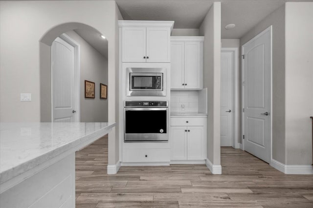 2653 Vermont Ave, Clovis, CA 93619 - kitchen featuring stainless steel appliances, white cabinetry, light wood-type flooring, light stone countertops, and arched walkways