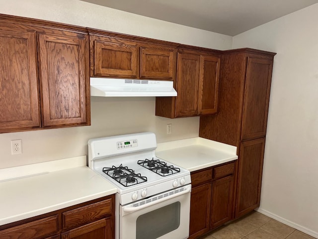 1836 Heidi Ave, Sanger, CA 93657 - kitchen with under cabinet range hood, light countertops, light tile patterned floors, white gas stove, and brown cabinetry