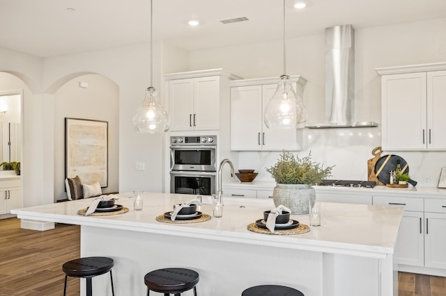 11182 N Via Ravenna Dr, Fresno, CA 93730 - kitchen featuring white cabinets, double oven, light countertops, wall chimney exhaust hood, and a breakfast bar area