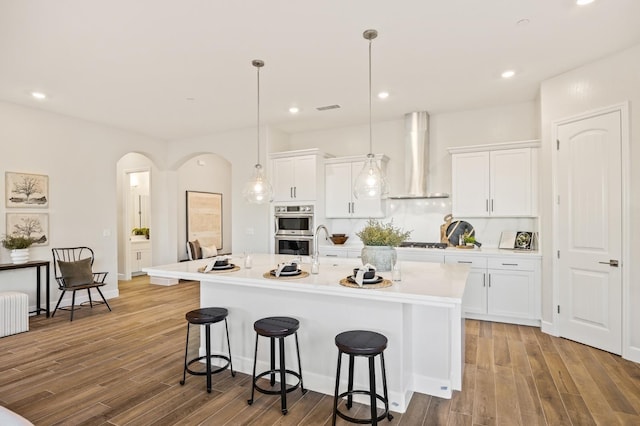 11182 N Via Ravenna Dr, Fresno, CA 93730 - kitchen featuring stainless steel appliances, wall chimney range hood, visible vents, arched walkways, and a kitchen bar