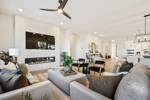 11182 N Via Ravenna Dr, Fresno, CA 93730 - living area with arched walkways, light wood finished floors, recessed lighting, and ceiling fan with notable chandelier