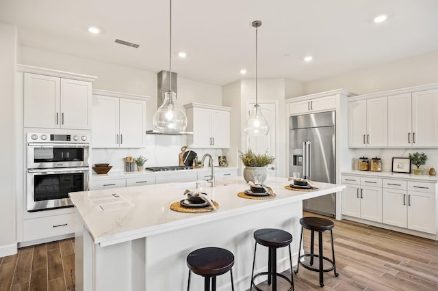 11182 N Via Ravenna Dr, Fresno, CA 93730 - kitchen featuring white cabinets, stainless steel appliances, wall chimney exhaust hood, a center island with sink, and a kitchen bar