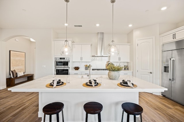11182 N Via Ravenna Dr, Fresno, CA 93730 - kitchen with a kitchen bar, wood finished floors, wall chimney range hood, and appliances with stainless steel finishes