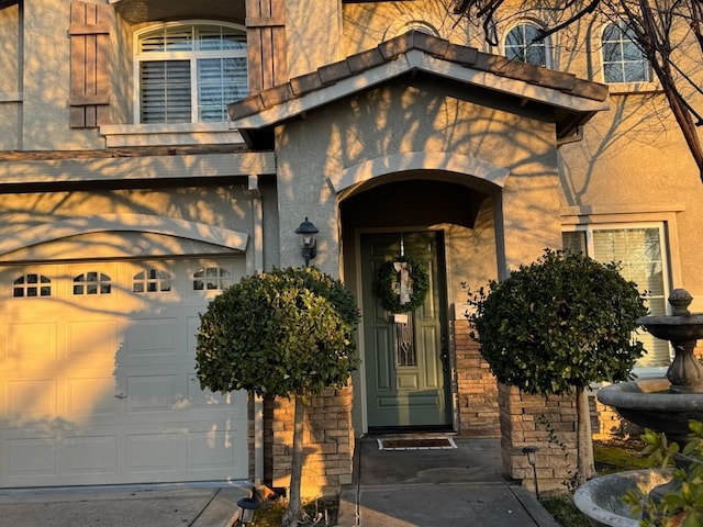 property entrance featuring stucco siding, stone siding, and a garage