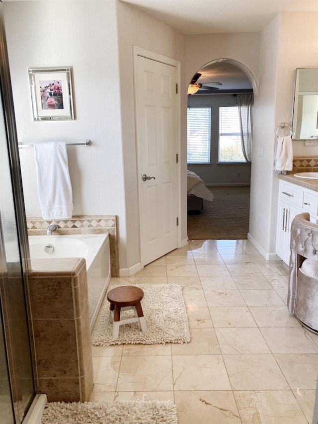 full bathroom featuring a bath, marble finish floor, baseboards, and vanity