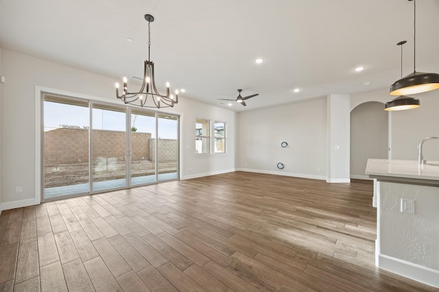 interior space featuring wood finished floors, ceiling fan with notable chandelier, arched walkways, baseboards, and recessed lighting