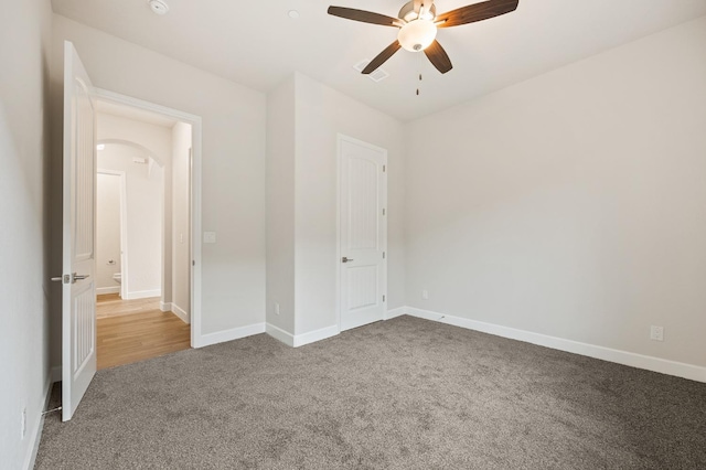 unfurnished bedroom featuring arched walkways, a ceiling fan, carpet flooring, and baseboards