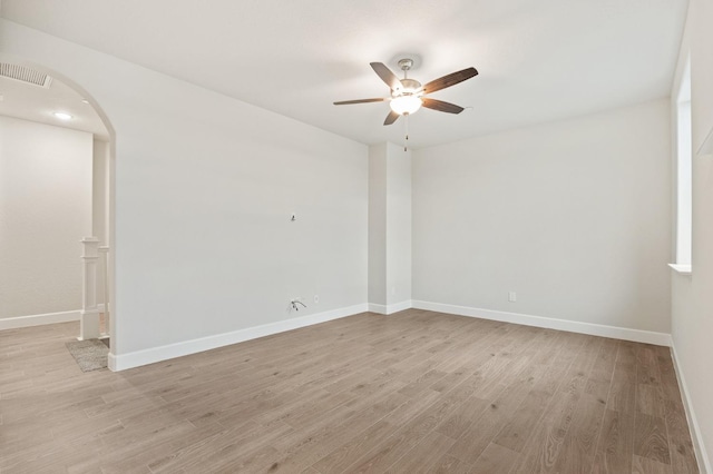 spare room with visible vents, a ceiling fan, arched walkways, light wood-style floors, and baseboards