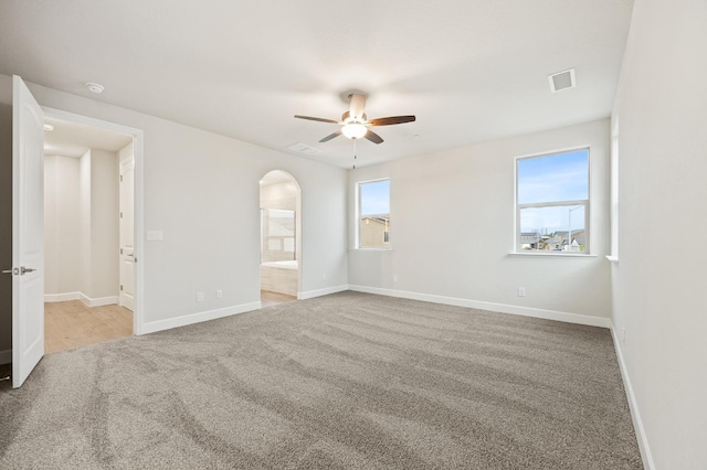 spare room with ceiling fan, arched walkways, baseboards, carpet flooring, and visible vents