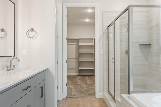 full bath with a spacious closet, vanity, wood finished floors, and a stall shower