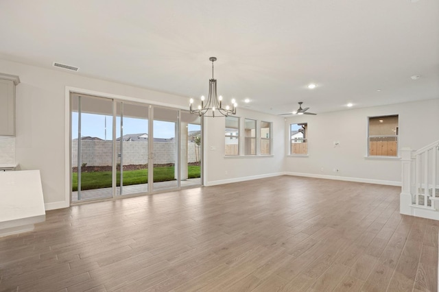 unfurnished living room with baseboards, ceiling fan with notable chandelier, visible vents, and light wood-style flooring
