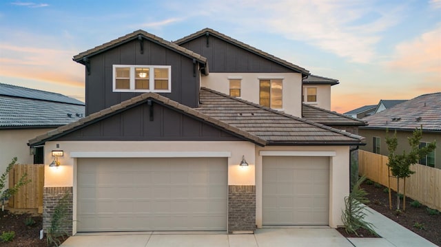view of front facade featuring a tiled roof, concrete driveway, fence, an attached garage, and board and batten siding