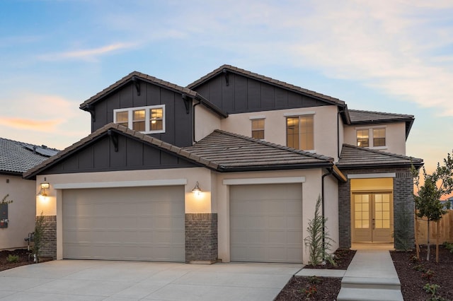 view of front of property with a tiled roof, board and batten siding, driveway, french doors, and a garage