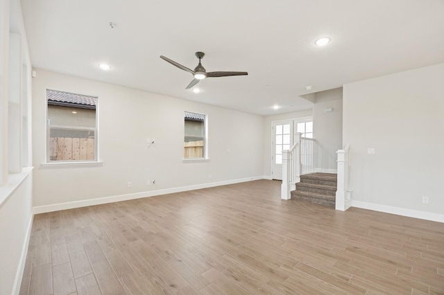 unfurnished living room featuring light wood finished floors, a ceiling fan, baseboards, and stairway