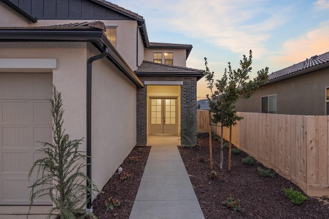 exterior entry at dusk with fence, french doors, a garage, and stucco siding
