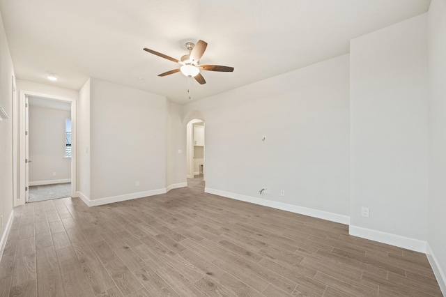 spare room featuring arched walkways, light wood-type flooring, baseboards, and ceiling fan