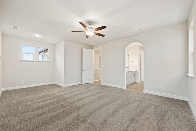 unfurnished bedroom with light carpet, baseboards, visible vents, and arched walkways