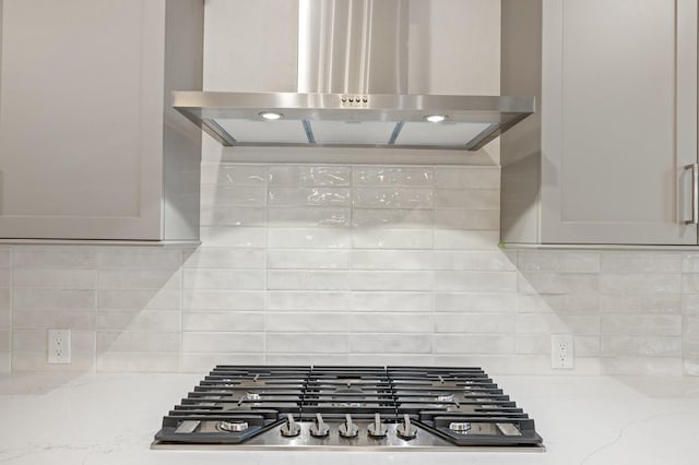 details featuring wall chimney exhaust hood, decorative backsplash, stainless steel gas stovetop, and light stone counters